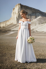 Fototapeta na wymiar Beautiful bride in a wedding dress with a bouquet standing against white rock