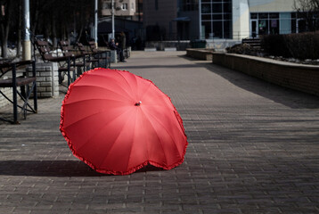 a red umbrella lies outside on a stone sidewalk on a spring autumn summer sunny day