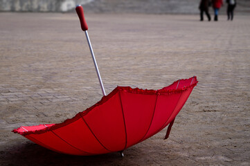 the red umbrella is lying on the street on the stone pavement on a spring autumn summer cloudy day...