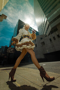 Ground view of an attactive young woman in a coffee filter coat, with a handbag and sunglasses both made of coffee beans, in front of buildings in the city