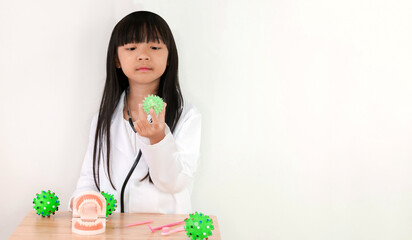 Asian child girl playing as a dentist holding a tooth decaying germ in her hand on a white background with copy space