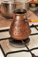 Cooking black coffee in a copper cezve on a gas stove in the kitchen at home