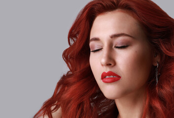 Close-up of beautiful young woman with red hair posing over grey background. 