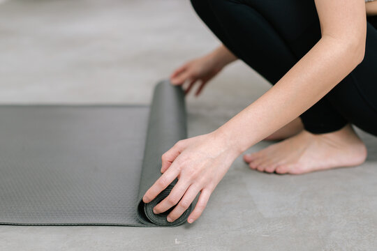 Hands of an attractive young woman folding black yoga or fitness mat after working out at home in living room or in yoga studio. Close up view photo