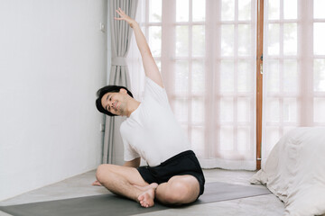 Training At Home. Sporty man doing yoga while watching online tutorial on laptop, exercising in living room, free space