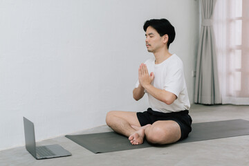 Training At Home. Sporty man doing yoga while watching online tutorial on laptop, exercising in living room, free space