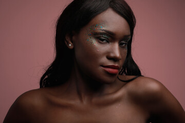 Fototapeta premium Portrait of young black woman posing in the studio, with glittery make-up.