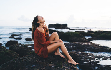 Young positive woman sitting on seashore rocks