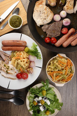 Mix meet chicken beef steak sausage tomato onion garlic fry grill metal pan colorful pasta green salad cheese olive mint basil pesto sauce board knife fork spoon sliced served plate wooden table