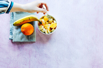Healthy breakfast of a bowl of fruit. Healthy meal orange with banana. Hand holding fork