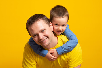 Happy father's day! Emotional dad and son hugging on yellow background.