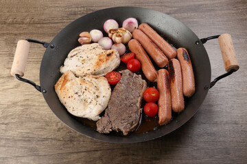 Mix meet pan chicken breast beef steak sausage tomato onion garlic oil fry grill on metal frying pan two wood handle on rustic wooden background