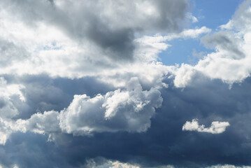 Fototapeta na wymiar de gros nuages blancs encore au soleil se forment devant des nuages d'un gris sombre avec des trous de ciel bleu