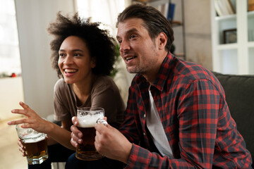 Boyfriend and girlfriend drinking beer at home. Happy couple watching sports game on tv.