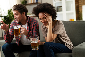 Boyfriend and girlfriend drinking beer at home. Happy couple watching sports game on tv.