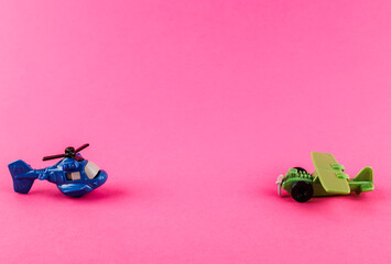 Small plastic airplane and helicopter with copy space on pink background.