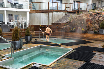 Man bathes or takes bath in small pool with hot water. Hot springs for bathing and wellness are...