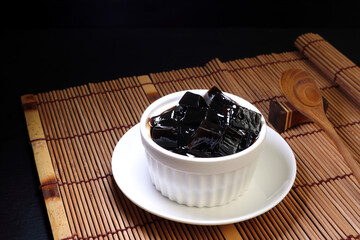 sweet grass jelly (Mesona chinensis) in a white bowl : southeast asia herbal popular dessert made by boiling the aged and slightly oxidized stalks with sugar.