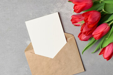 Card or invitation mockup with red tulips bouquet and envelope on grey concrete background