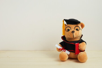 Cute teddy bear with nice graduation clothes and diploma on wooden table. School concept