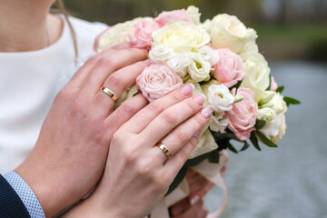 Bride and groom holding bridal bouquet of roses together. Wedding rings on a fingers.