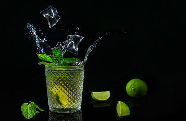Refreshing mojito cocktail with ices cubes and splash on dark background.Summer drink with fresh limes and mint with copy space.