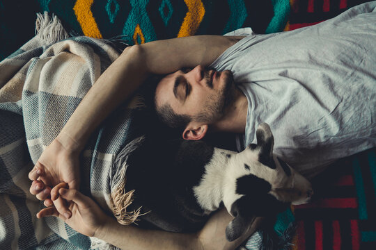 Midsection Of Man Sleeping On Bed At Home With Dog. Overhead