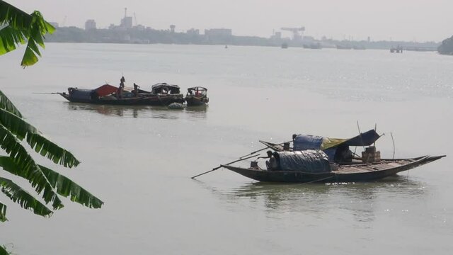 A group of fishermen working on boats on a river under a cloudy sky in Begal, India shot in HD