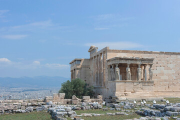 Obraz premium Ancient temple with beautiful Caryatids on Acropolis hill, famous tourist attraction in Athens, Greece, in sunny summer day