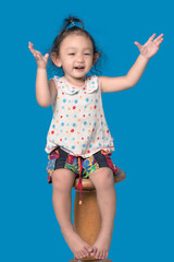 A girl sitting on a wooden chair with a blue cloth in the background.