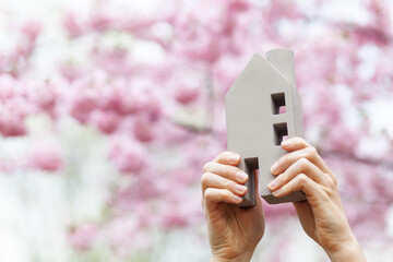 Real estate in the suburbs. House model in hands. Home in a blooming garden.