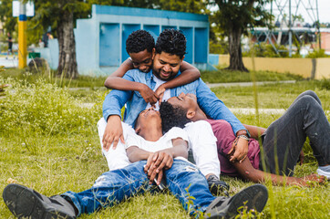 Dominican Latino origin man celebrating father's day with his children in the park, dark-skinned family having fun, children hugging their father sitting in the park - obrazy, fototapety, plakaty