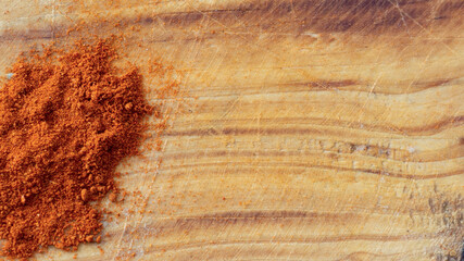 Red paprika powder over a rustic wooden cutting board background with copy space