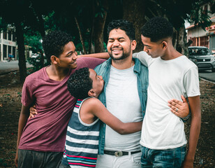 Dominican Latino origin man celebrating father's day with his children , in the park, dark-skinned family having fun, children hugging their father - obrazy, fototapety, plakaty