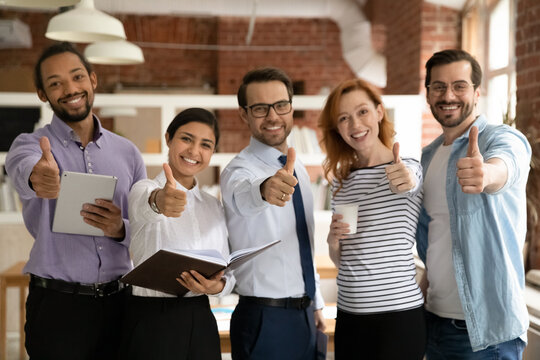 Smiling diverse employees group showing thumbs up and looking at camera, excited satisfied workers businesspeople recommending best corporate service, great career opportunities, human resources - Powered by Adobe