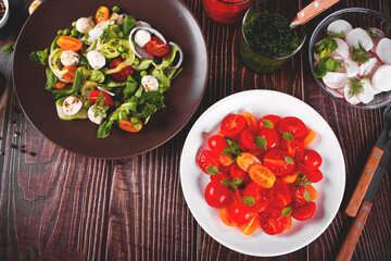 salads of fresh cherry tomatoes with basil, mozzarella, greens and radish on the dinner table