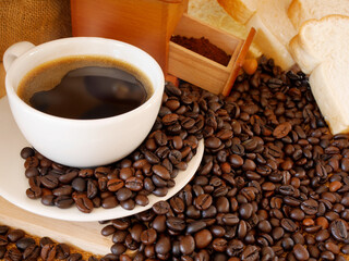 The aroma hot coffee in white cup for drink in this morning with coffee powder and coffee beans and some bread for eat in breakfast