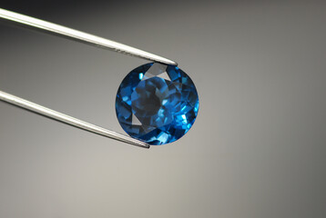 Natural London dark blue color topaz round faceted gemstone. Heated, treated, irradiated. For jewelry making loose setting in tweezers. Gray gradient background. Gemology theme.