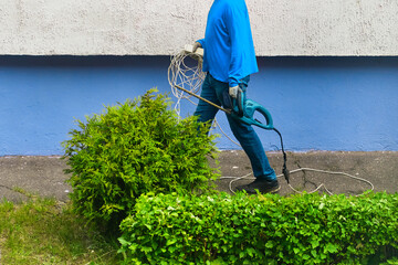 worker holds bush clipper and an electric wire extension cord