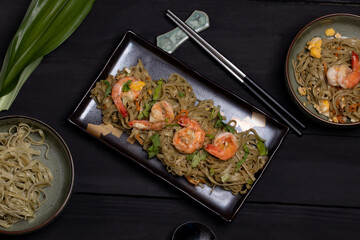 Fried yakisoba noodles with prawns in a black flat lay dish.