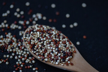 Quinoa in a wooden spoon on a black background
