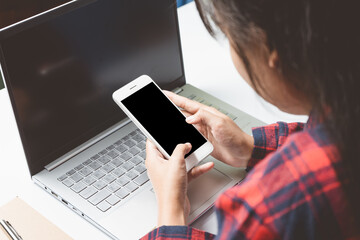 Asian young woman shopping online, choose clothes on mobile phone with labtop on a white desk in the living room. Financial transactions through smartphones. Easy shopping and covenient concept