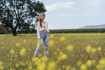 Young woman posing happily in a field of yellow flowers