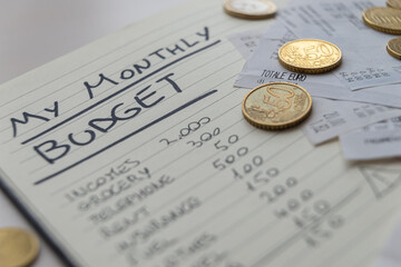 Page of notepads with monthly expense budgets, with receipts and invoices beside them, and coins. Monthly budget.
