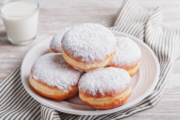 Delicious strawberry jam filled berliner doughnuts on white plate and glass of milk on wooden table top overhead