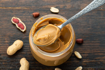 Peanut butter in an open jar and heap of nuts on wood background.