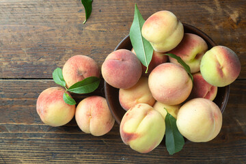 Ripe peaches with leaves in a clay bowl on a wooden table.