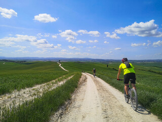 Ragazzo fa escursione in bicicletta sul sentiero tra i campi di grano in collina in toscana