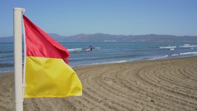 Red and yellow guard flag on sandy beach against swimming people.