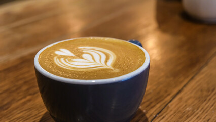 A Blue coffee cup with a steamed milk leaf, Placed on a wooden counter in a cafe. Coffee Art.